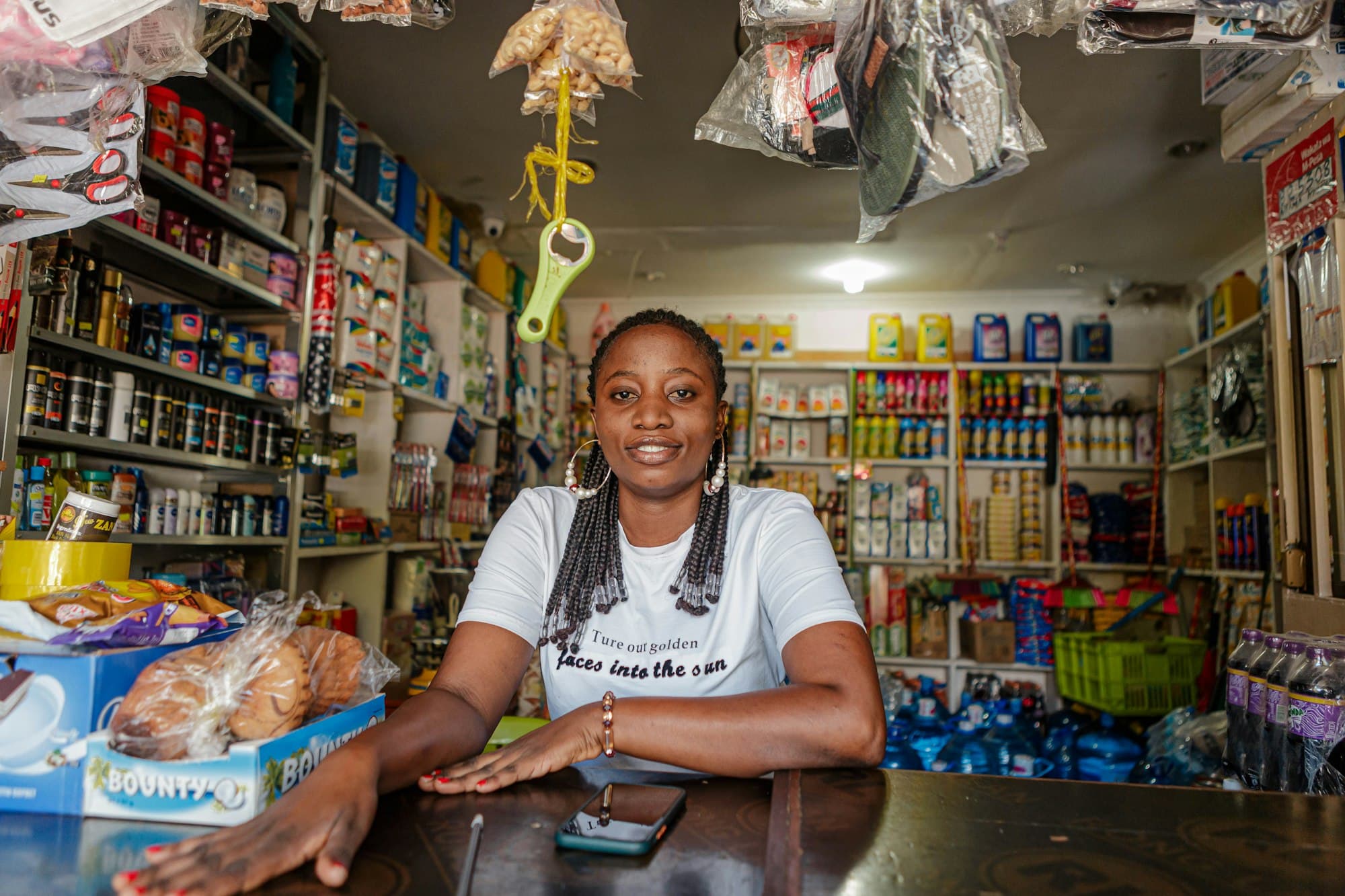 Smiling woman behind the counter of a small, well-stocked neighbourhood shop