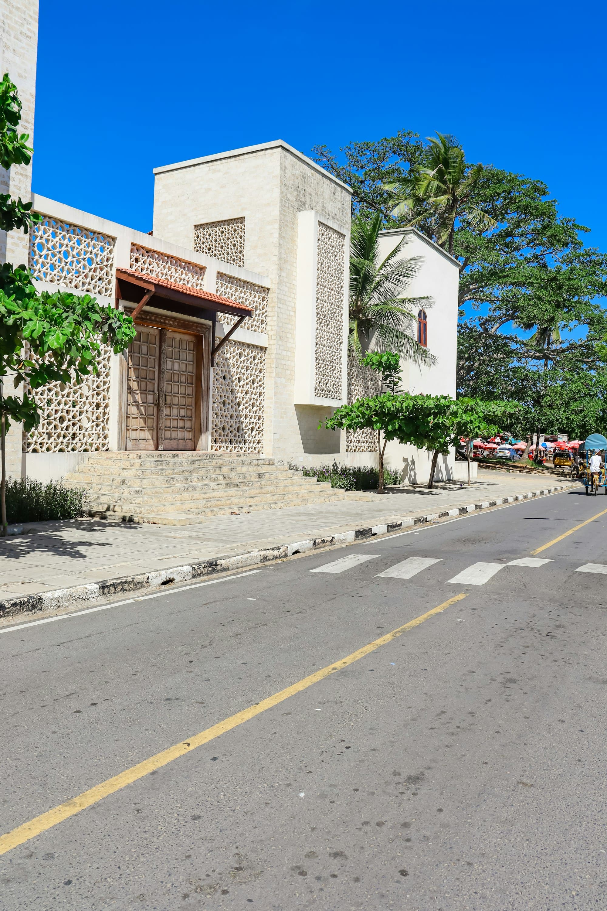 Sunny street on Mama Ngina Drive in Mombasa, lined with a carved-lattice stone building and palm trees
