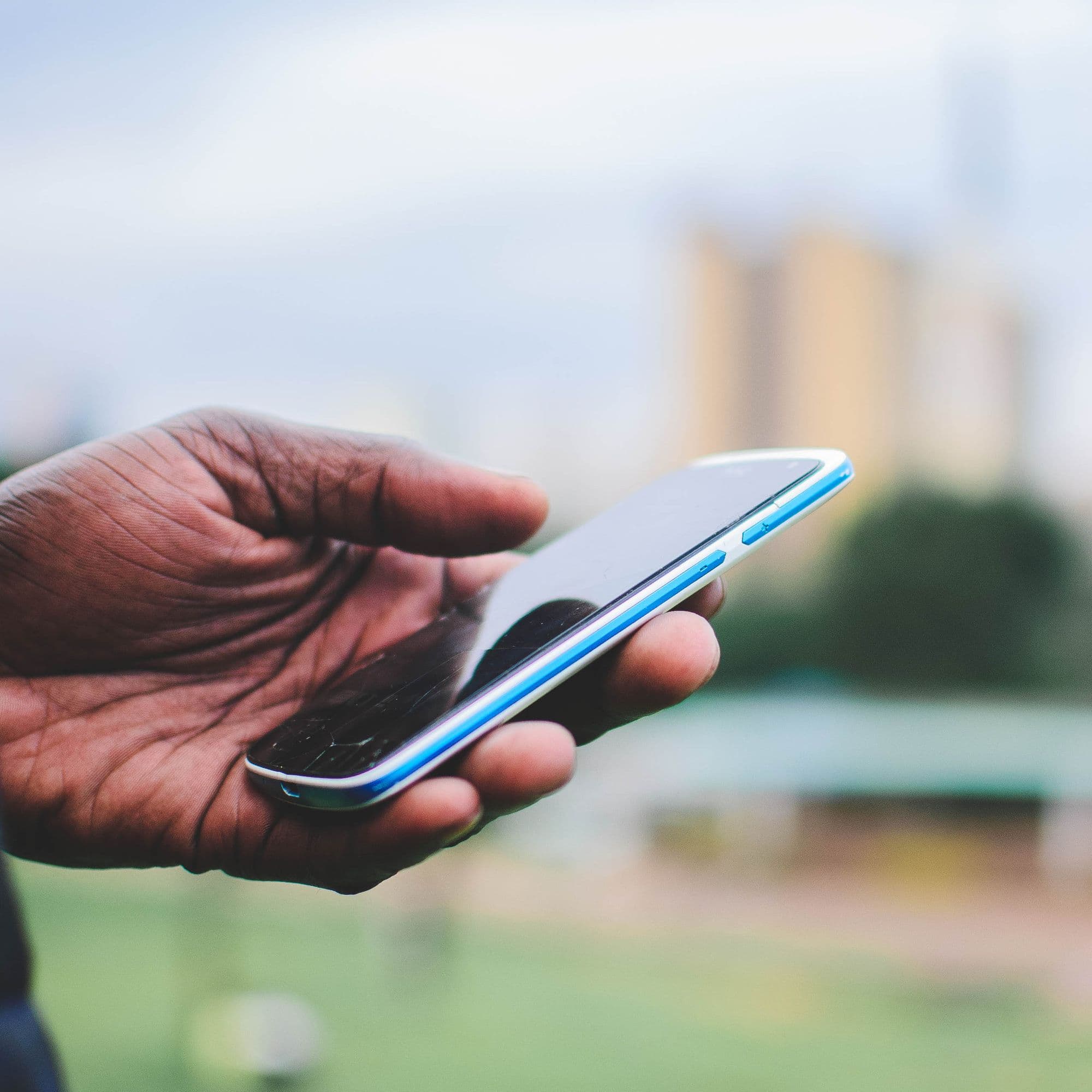 Close-up of a hand holding a smartphone outdoors with a blurred city background